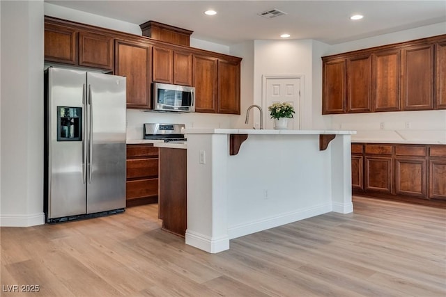 kitchen featuring light wood finished floors, visible vents, a center island with sink, light countertops, and appliances with stainless steel finishes