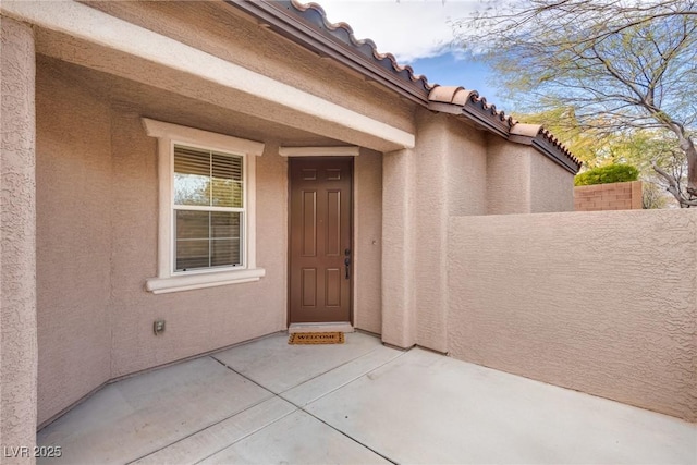 view of exterior entry featuring a patio area, stucco siding, and fence