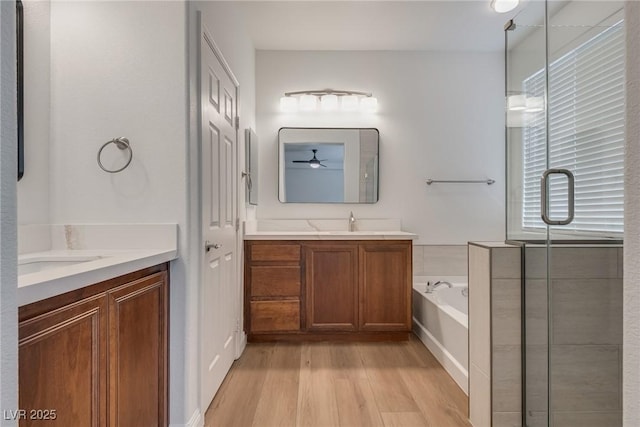 bathroom with two vanities, a ceiling fan, a sink, wood finished floors, and a bath