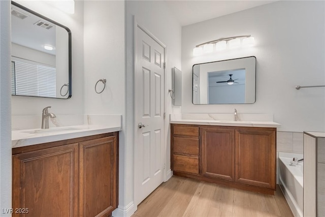 bathroom featuring a sink, two vanities, wood finished floors, and a ceiling fan