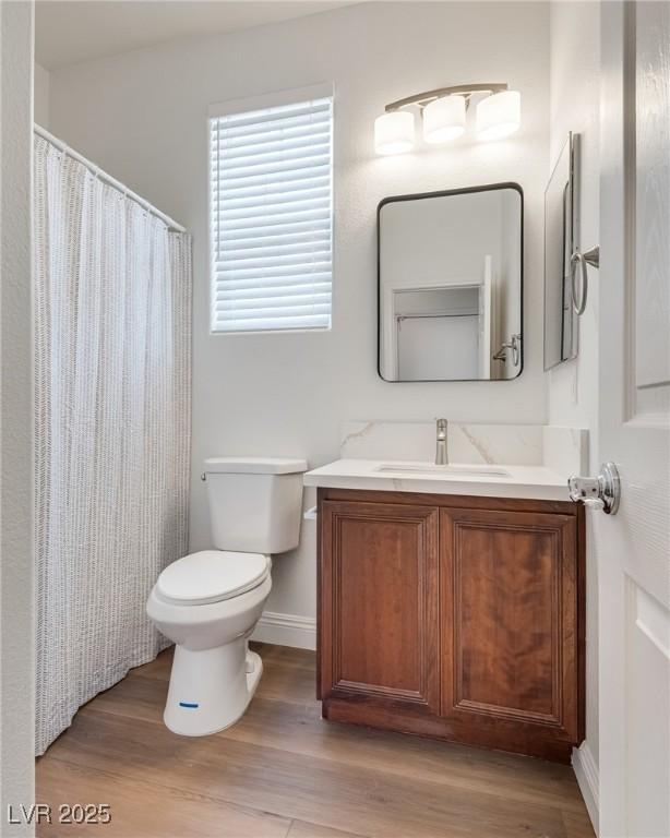 bathroom with vanity, wood finished floors, baseboards, curtained shower, and toilet