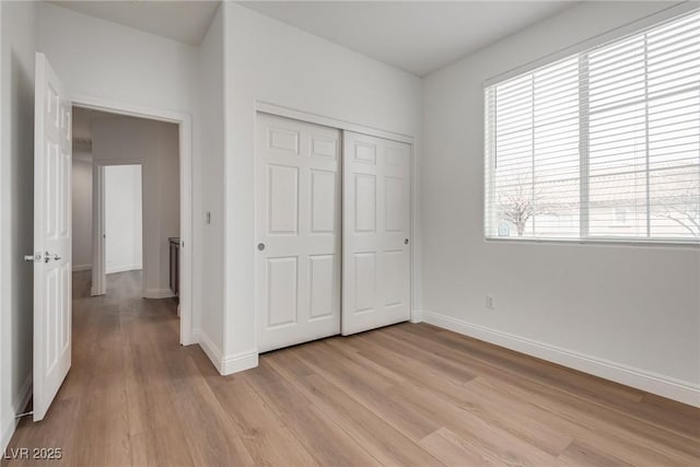 unfurnished bedroom featuring a closet, light wood-type flooring, and baseboards