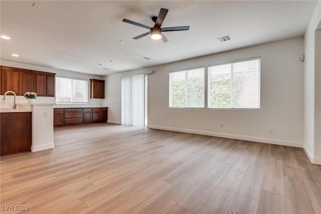 unfurnished living room with a ceiling fan, baseboards, visible vents, light wood-style flooring, and a sink