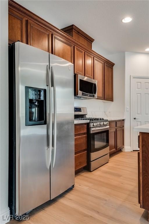 kitchen with stainless steel appliances, light countertops, brown cabinetry, and light wood finished floors