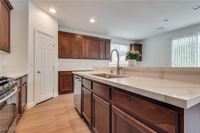 kitchen with visible vents, a sink, light stone counters, stainless steel appliances, and light wood-style floors