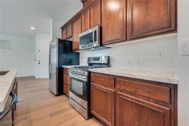 kitchen with light stone counters, appliances with stainless steel finishes, light wood-type flooring, and baseboards