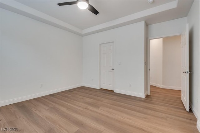 unfurnished bedroom with light wood-style flooring, a tray ceiling, baseboards, and ceiling fan