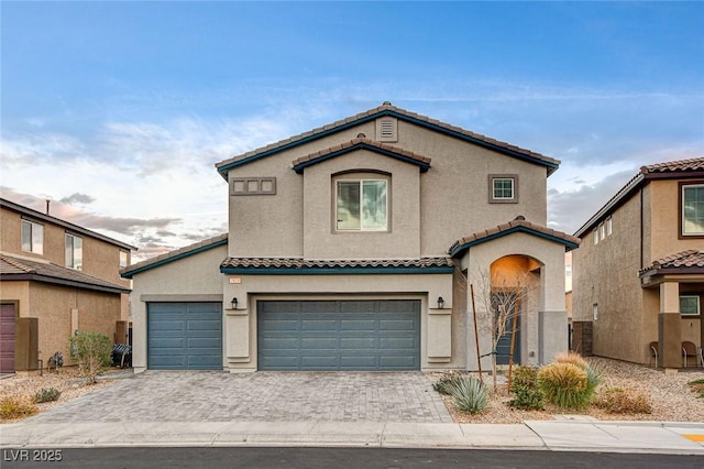 mediterranean / spanish-style home featuring a garage, decorative driveway, stucco siding, and a tile roof