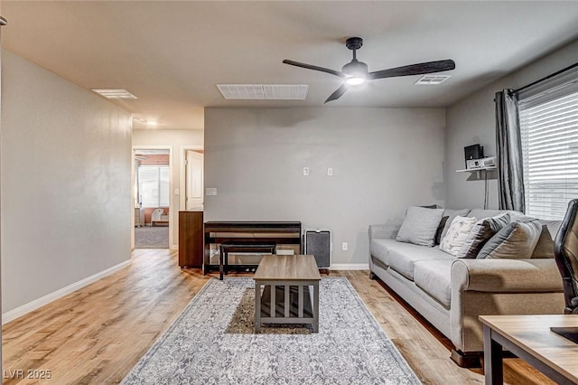 living area featuring light wood-style flooring, a ceiling fan, visible vents, and baseboards