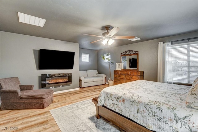 bedroom with visible vents, multiple windows, a glass covered fireplace, and wood finished floors