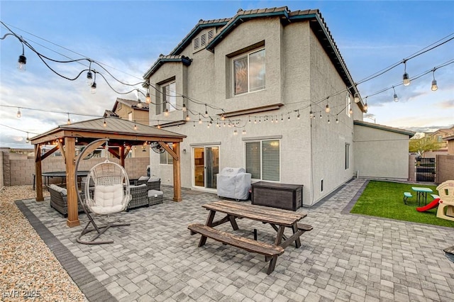 rear view of house with a gazebo, stucco siding, a fenced backyard, and a patio area