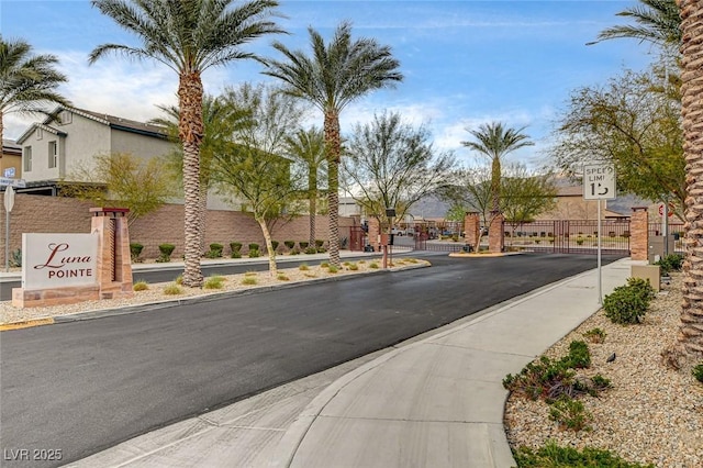 view of street featuring a gate, traffic signs, sidewalks, curbs, and a gated entry