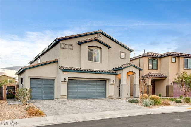 mediterranean / spanish-style home with fence, a tiled roof, stucco siding, decorative driveway, and a garage