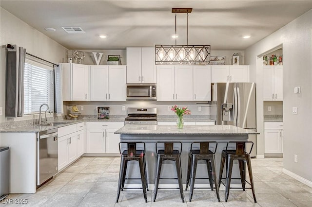 kitchen with visible vents, a sink, stainless steel appliances, white cabinets, and a kitchen breakfast bar