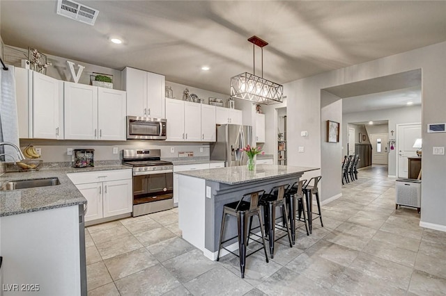 kitchen featuring visible vents, a kitchen island, a breakfast bar, stainless steel appliances, and a sink