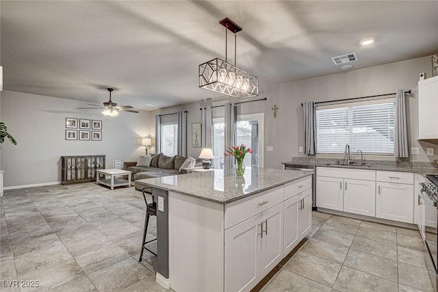 kitchen featuring a ceiling fan, visible vents, a kitchen island, a sink, and white cabinetry