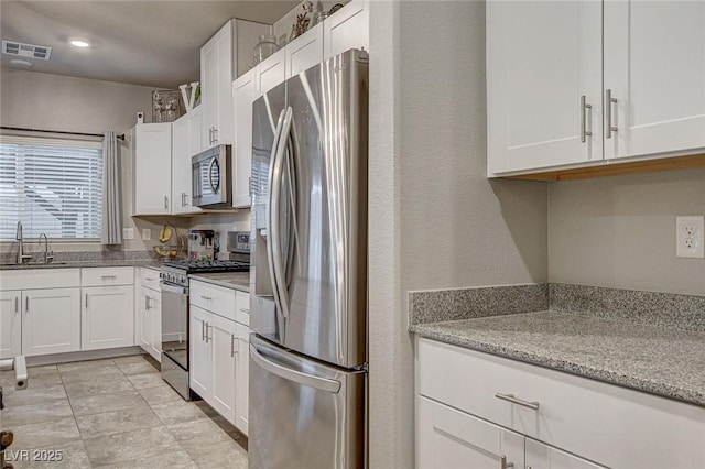 kitchen with visible vents, light stone countertops, appliances with stainless steel finishes, white cabinets, and a sink