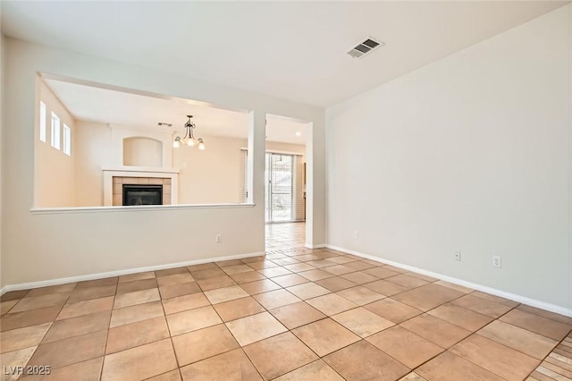 empty room with baseboards, visible vents, light tile patterned flooring, a tiled fireplace, and a notable chandelier