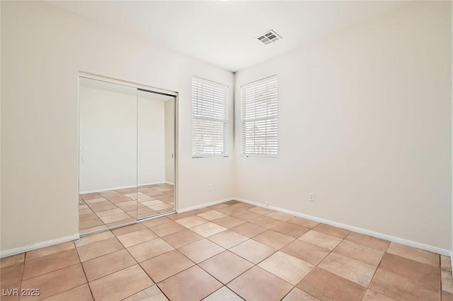 unfurnished bedroom featuring light tile patterned flooring, baseboards, visible vents, and a closet