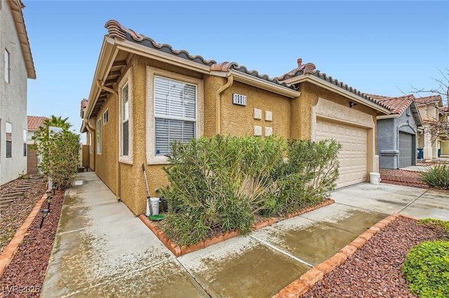 view of front of property with concrete driveway, a tiled roof, an attached garage, and stucco siding