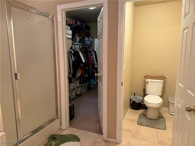 full bathroom featuring tile patterned flooring, a walk in closet, toilet, and a stall shower