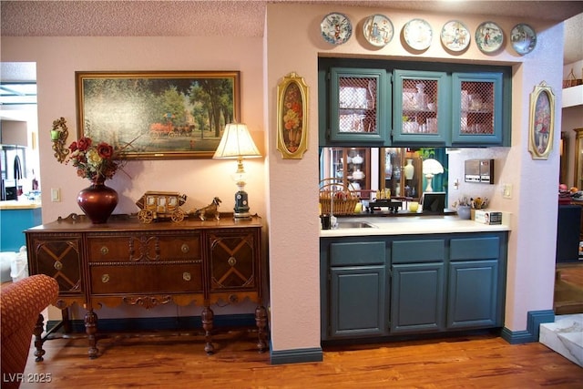 bar with a sink, light wood-style floors, stainless steel fridge, and a textured ceiling