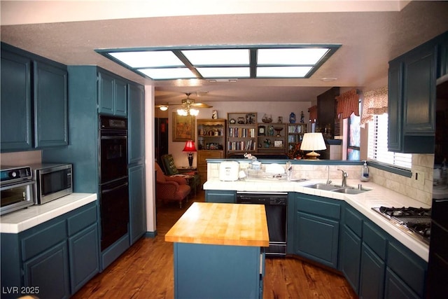 kitchen featuring wooden counters, a peninsula, blue cabinetry, a sink, and black appliances