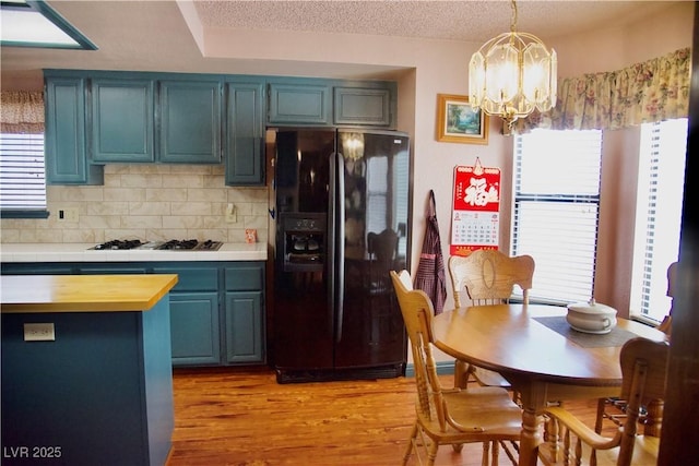 kitchen with black fridge, blue cabinetry, gas stovetop, and an inviting chandelier