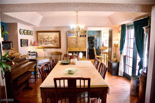 dining space featuring a notable chandelier, wood finished floors, vaulted ceiling, and a textured ceiling