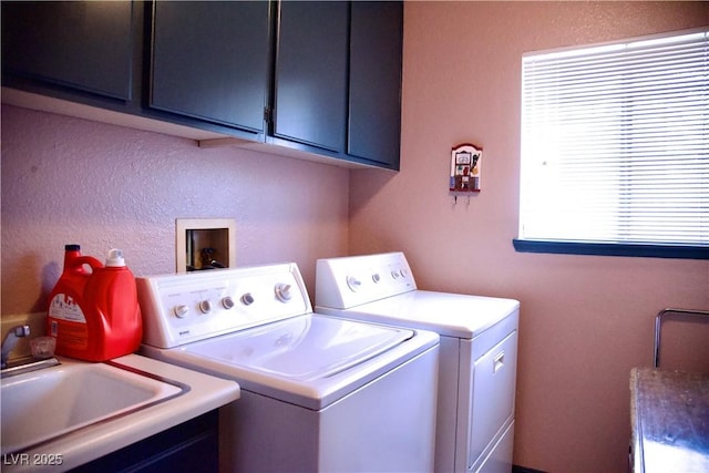 laundry area featuring a sink, cabinet space, a textured wall, and separate washer and dryer