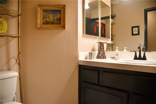 bathroom featuring toilet, vanity, and a textured wall