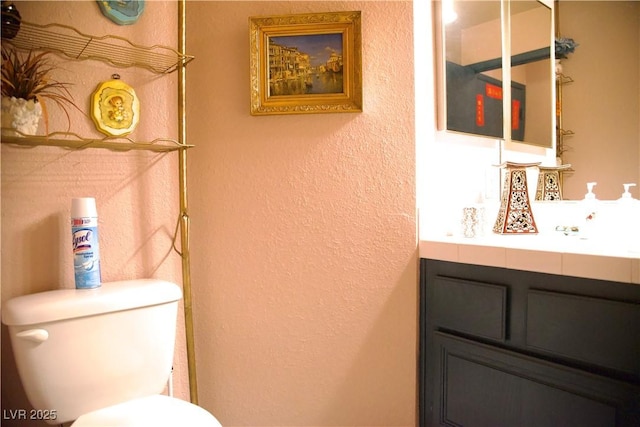 bathroom featuring toilet, vanity, and a textured wall