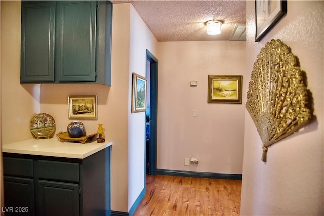 corridor featuring light wood finished floors, a textured ceiling, and baseboards