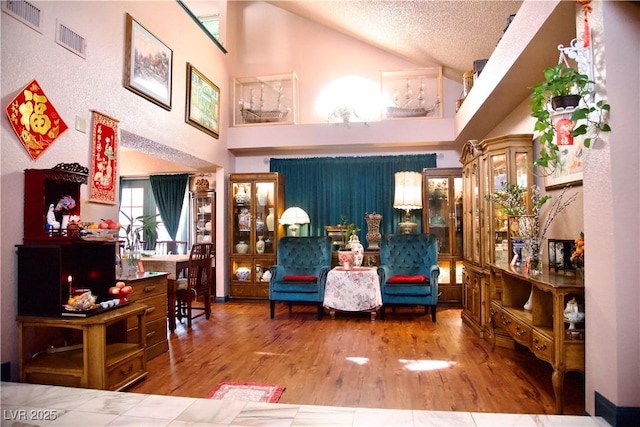 living area featuring high vaulted ceiling, visible vents, a textured ceiling, and wood finished floors