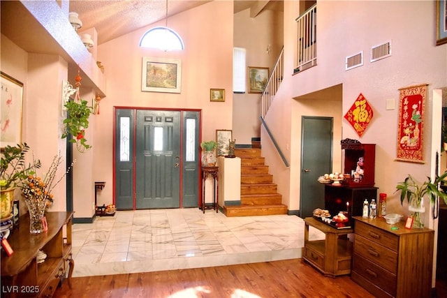 foyer featuring visible vents, stairway, high vaulted ceiling, and wood finished floors