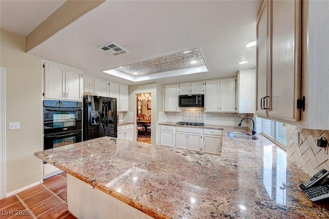 kitchen with visible vents, black appliances, a sink, a peninsula, and a raised ceiling