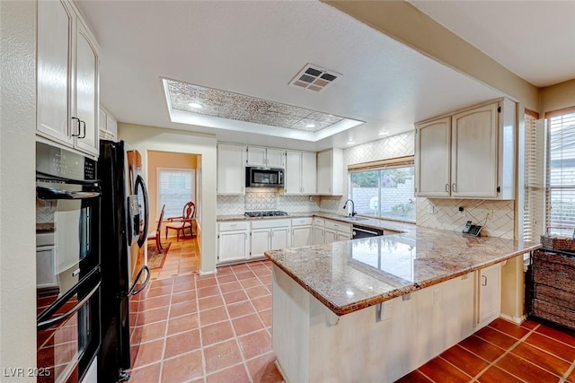 kitchen with visible vents, a tray ceiling, a peninsula, light tile patterned flooring, and black appliances