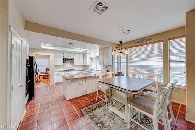 interior space featuring tile patterned floors, visible vents, a tray ceiling, baseboards, and a chandelier