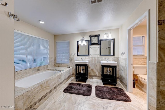 bathroom with visible vents, toilet, a bath, tile walls, and a sink