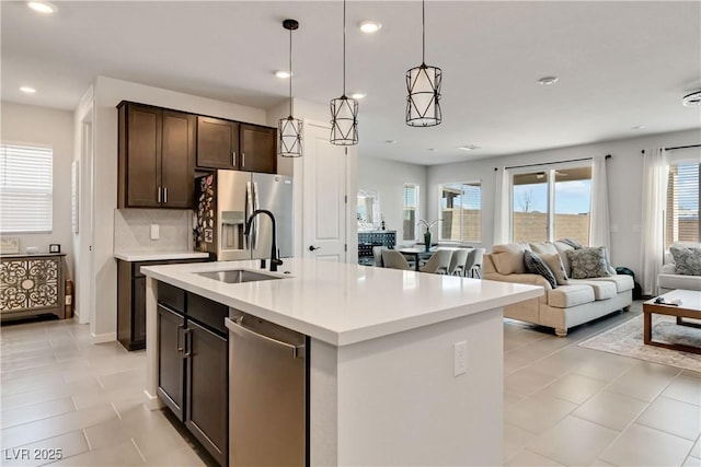 kitchen with dark brown cabinets, open floor plan, light countertops, stainless steel fridge, and a sink