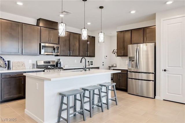 kitchen featuring a kitchen island with sink, a sink, stainless steel appliances, light countertops, and dark brown cabinets