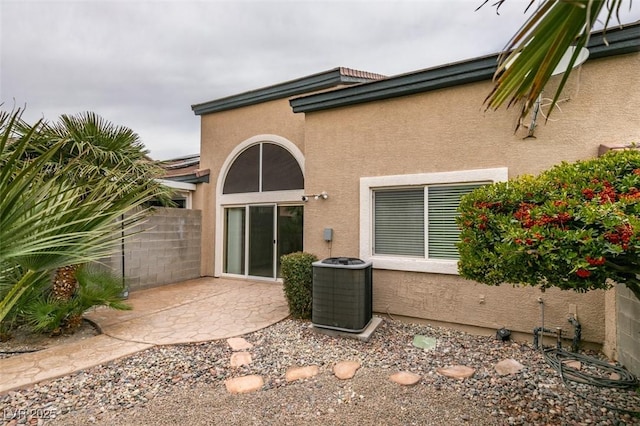 rear view of house featuring a patio, central AC unit, fence, and stucco siding