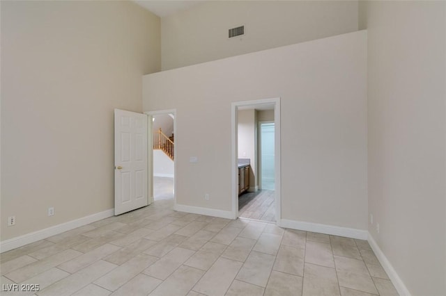 empty room featuring visible vents, baseboards, and a towering ceiling