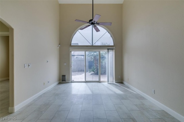 unfurnished room featuring a high ceiling, a ceiling fan, arched walkways, and baseboards