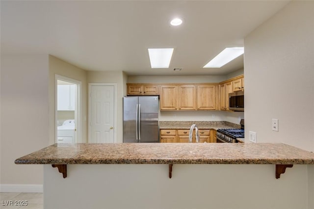 kitchen featuring a kitchen breakfast bar, washer / clothes dryer, appliances with stainless steel finishes, and a peninsula