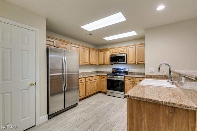 kitchen with light wood-style flooring, a sink, light stone counters, appliances with stainless steel finishes, and a skylight