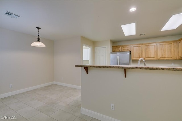 kitchen with baseboards, visible vents, freestanding refrigerator, a sink, and a kitchen breakfast bar