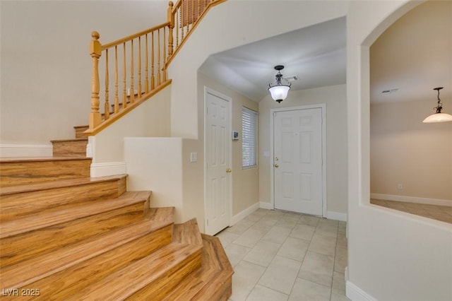 tiled entryway featuring arched walkways, stairway, visible vents, and baseboards