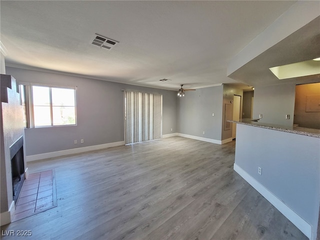 unfurnished living room featuring visible vents, a fireplace, ceiling fan, and wood finished floors