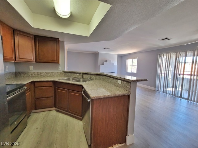 kitchen featuring visible vents, light wood finished floors, a peninsula, a sink, and stainless steel appliances